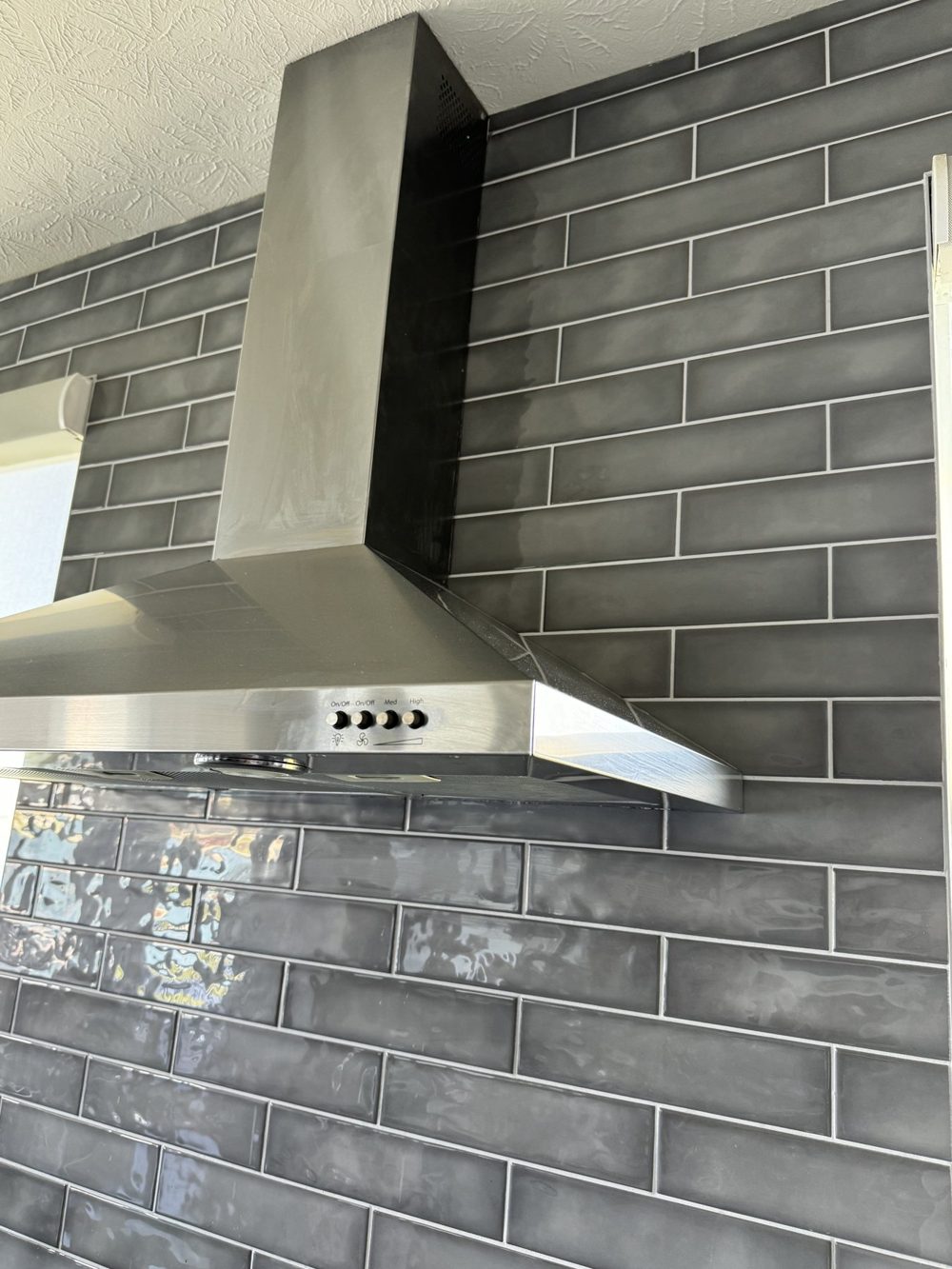 Grey subway tile backsplash behind a range and stainless hood