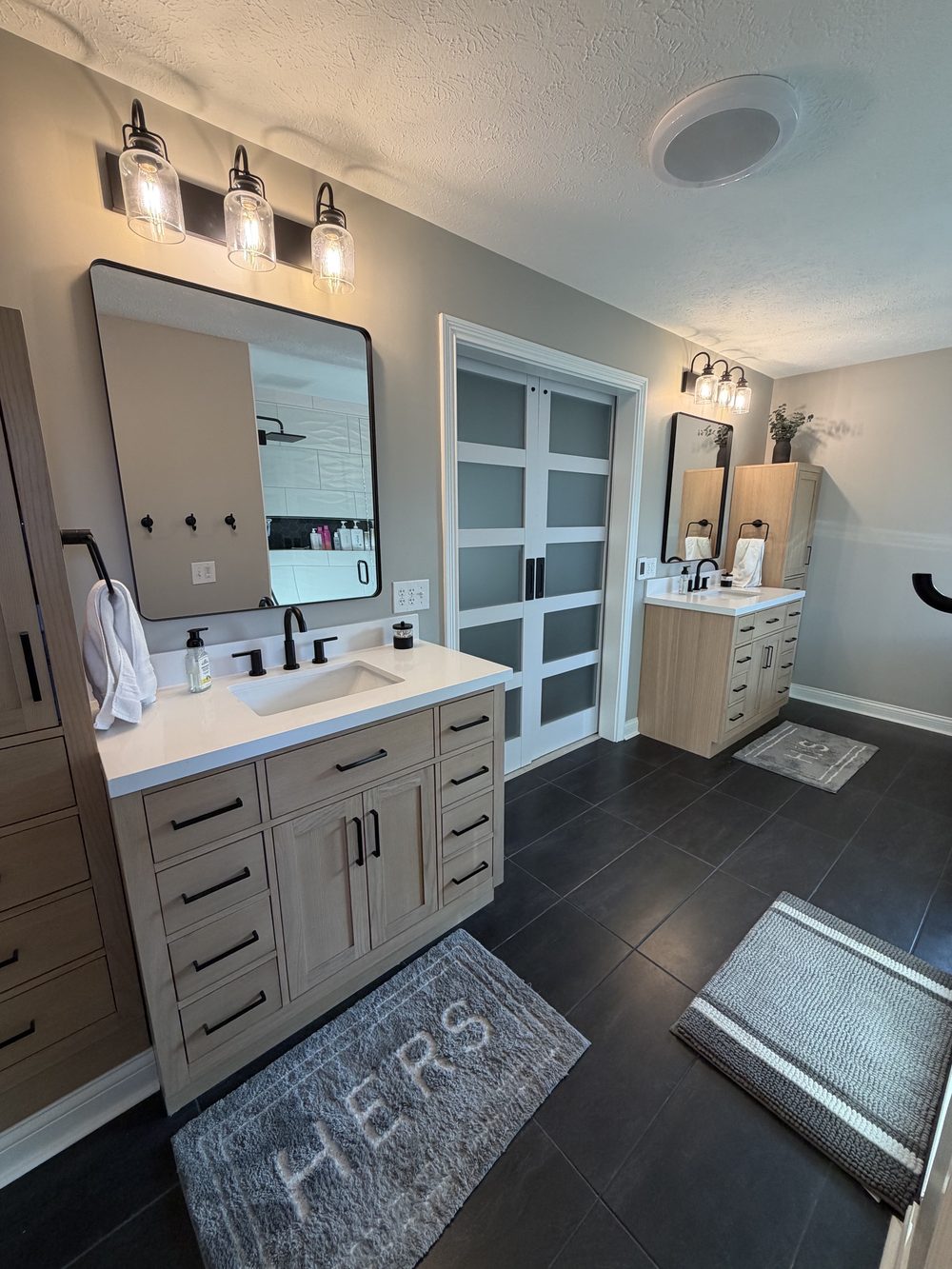 Primary bathroom vanity with a framed mirror, sconces and frosted glass doors