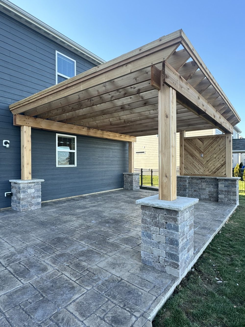 Covered patio with timber framing and stone columns over stamped concrete