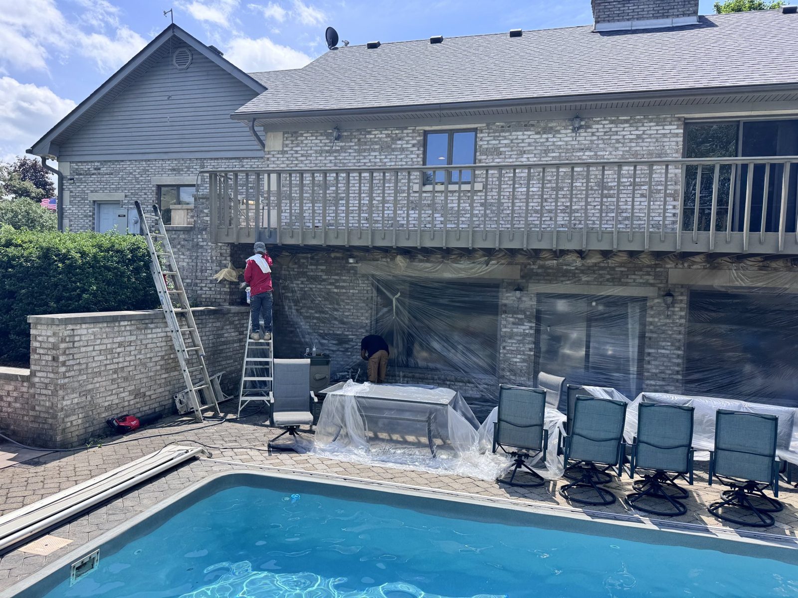 Crew on a ladder painting a two story exterior above a pool