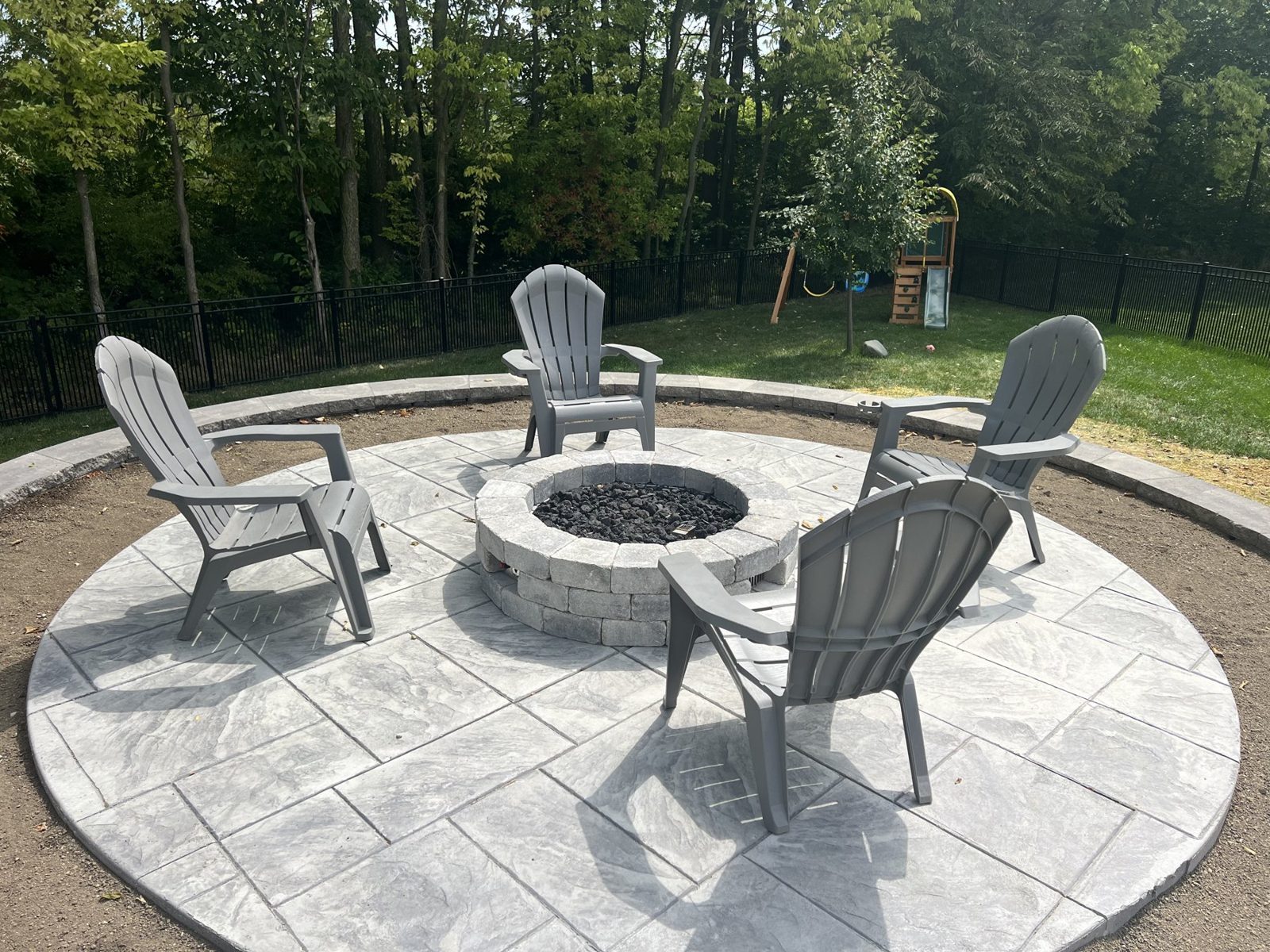 Round stamped patio with a fire pit ringed by adirondack chairs