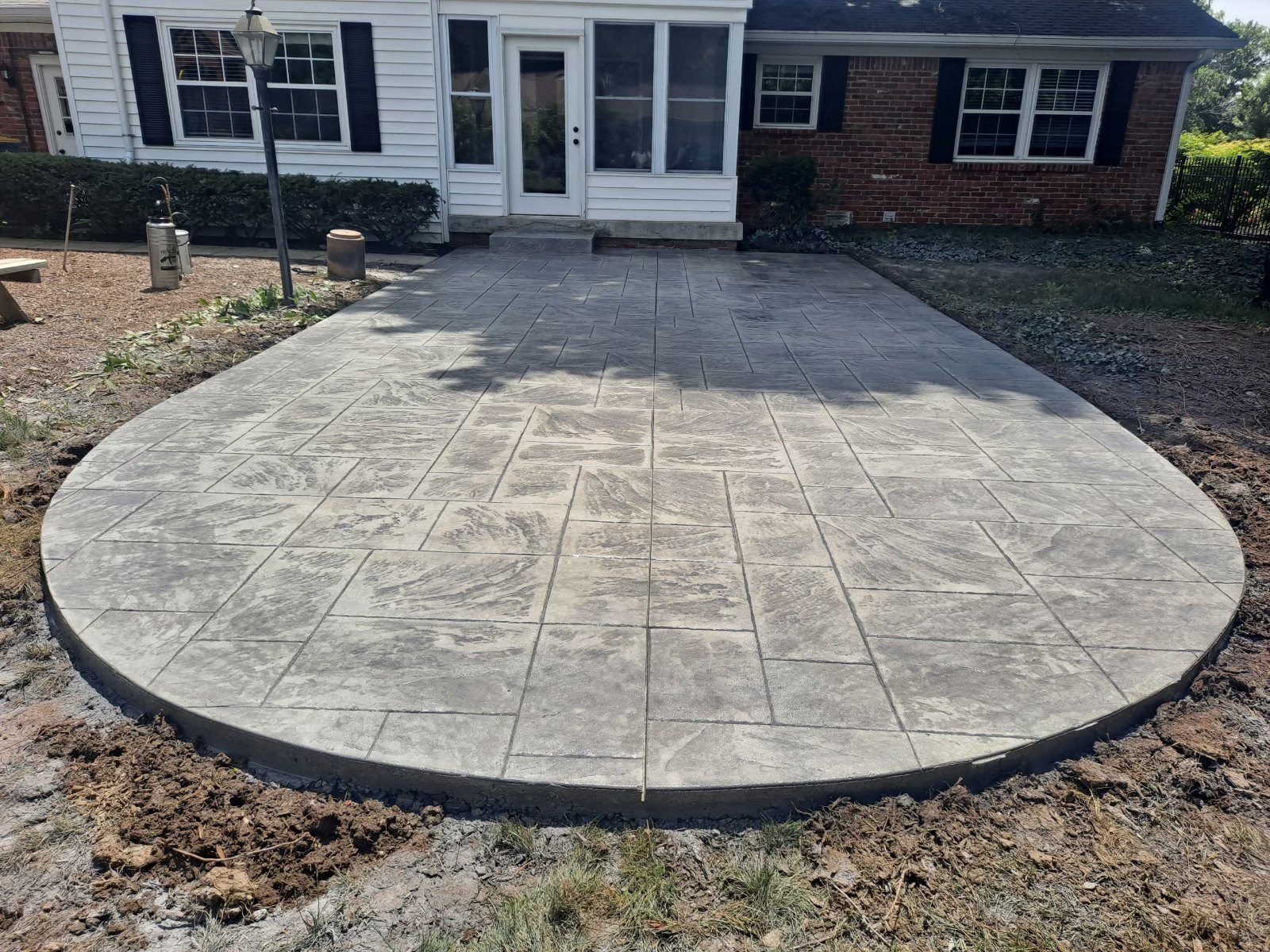 Large oval stamped concrete patio behind a brick home