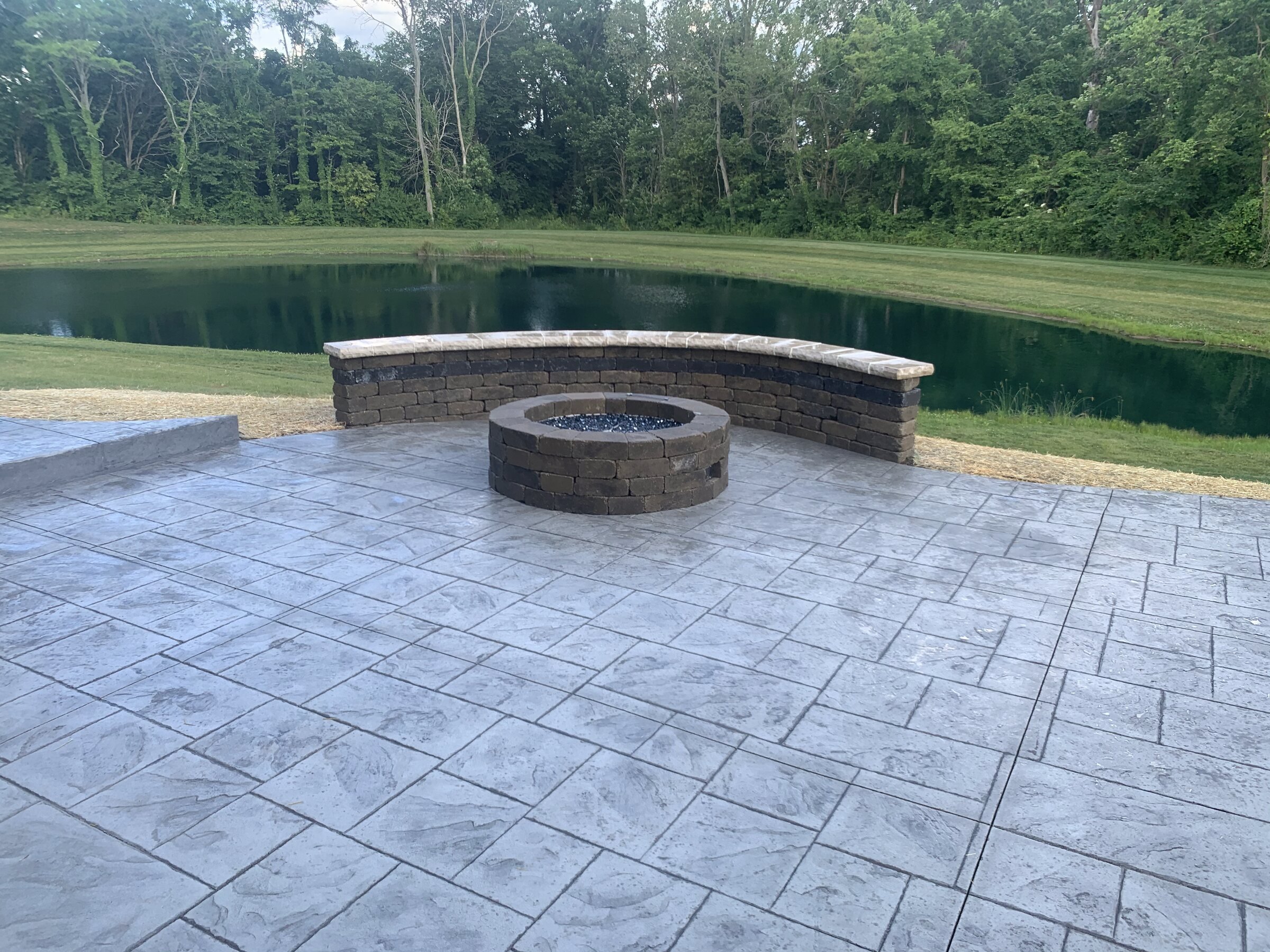 Stamped patio with a stone fire pit and curved sitting wall overlooking a pond