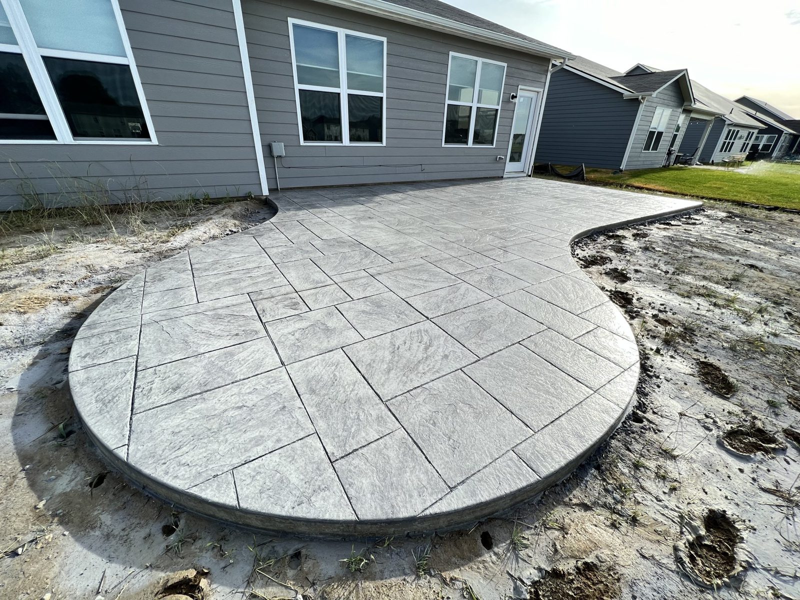 Freshly stamped curved patio being finished behind a home